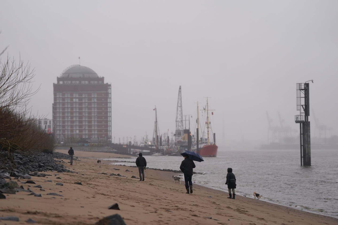 Passanten gehen im strömenden Regen am Elbstrand in Ovelgönne spazieren.